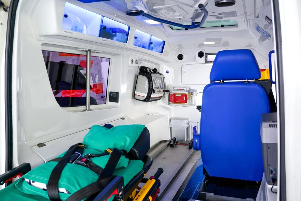 Modern ambulance with stretcher, blue seat and medical equipment for safe non-emergency medical transports.