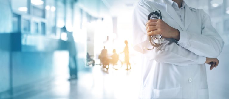 Læge på klinik med stetoskop, patienter i kørestol i baggrunden, støtte til lægebesøg.