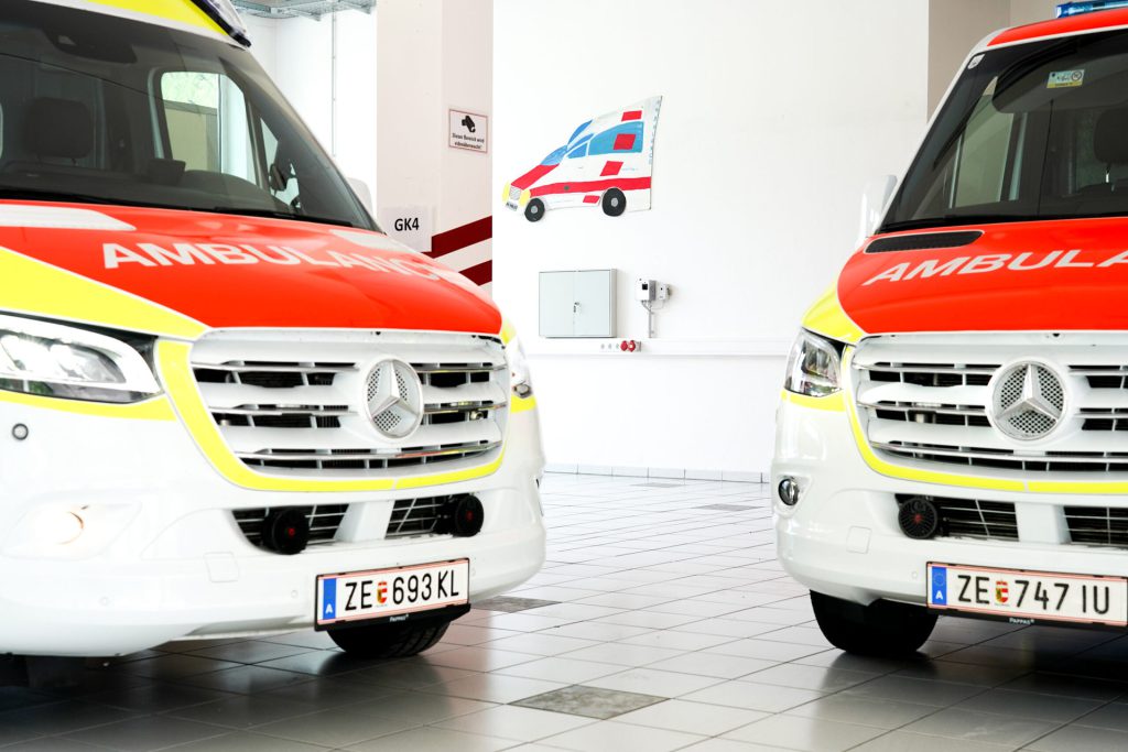 Two ambulances with red-and-yellow lettering in a modern hall.